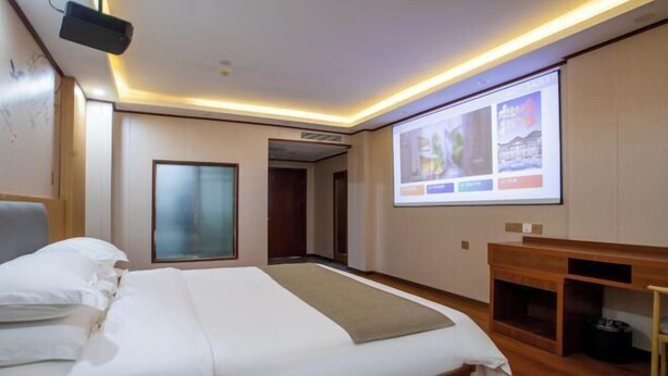 Una habitación de hotel con una cama, una pantalla de proyector y un escritorio de madera.