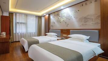 A hotel room with two beds, a wooden desk, a wall with a floral painting, and a curtain-covered window.