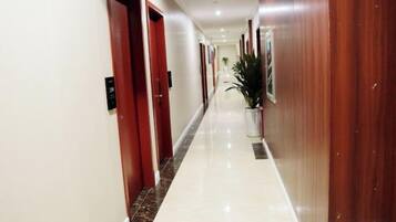 A hotel corridor with wooden doors, a potted plant, and a marble floor.