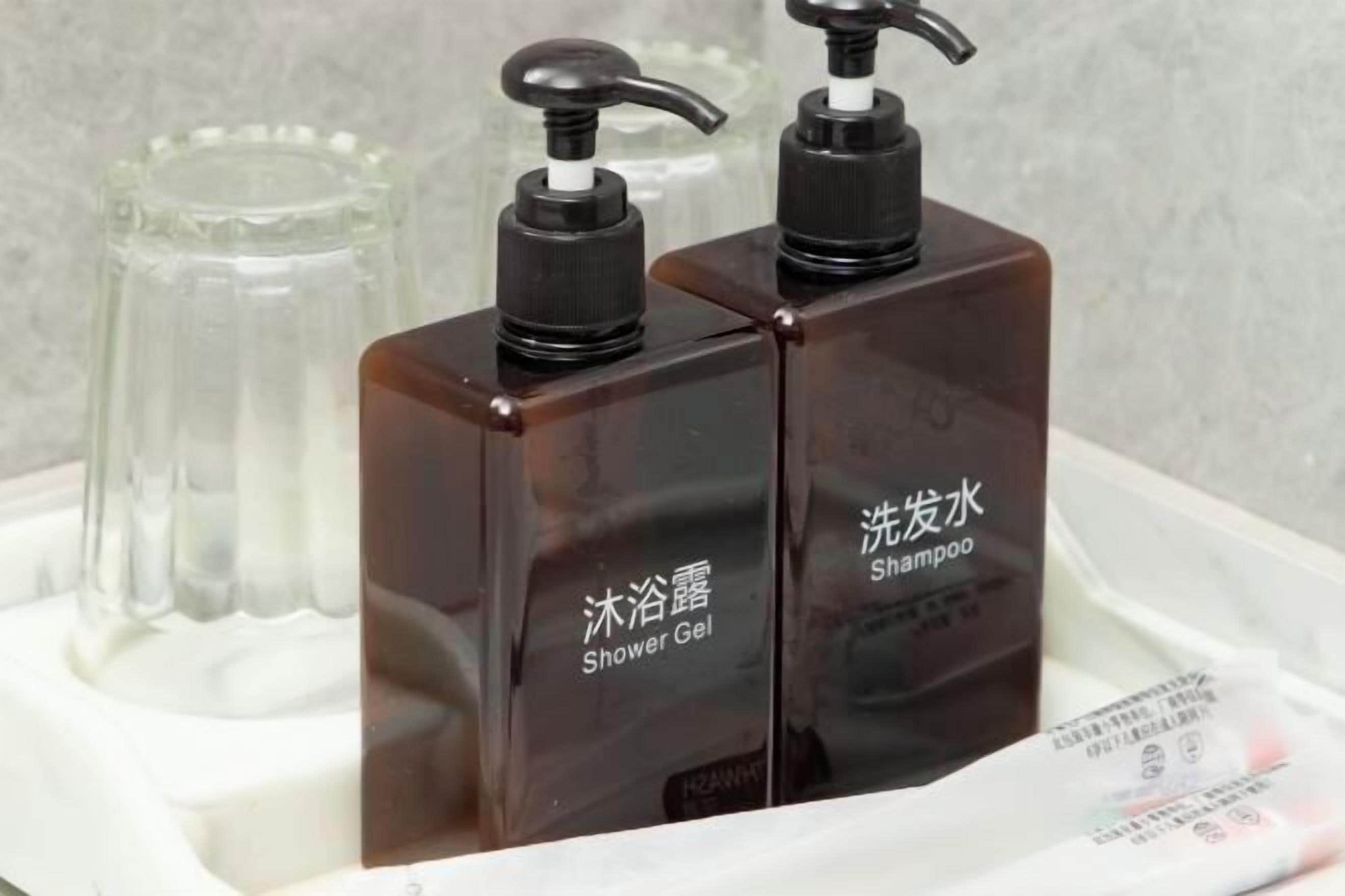 Two brown bottles with black pumps labeled "Shower Gel" and "Shampoo" on a white tray.