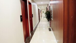 Un pasillo de hotel con puertas de madera, una planta en maceta y piso de baldosas.