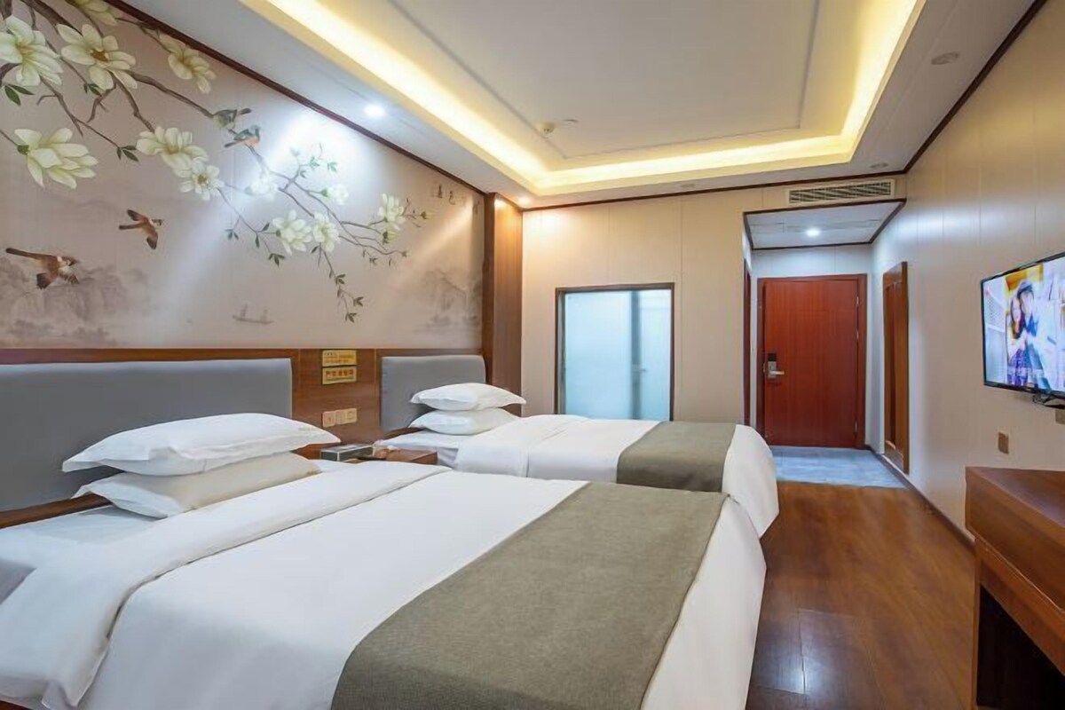 A hotel room with two beds, a television, and a wall with floral and bird artwork.