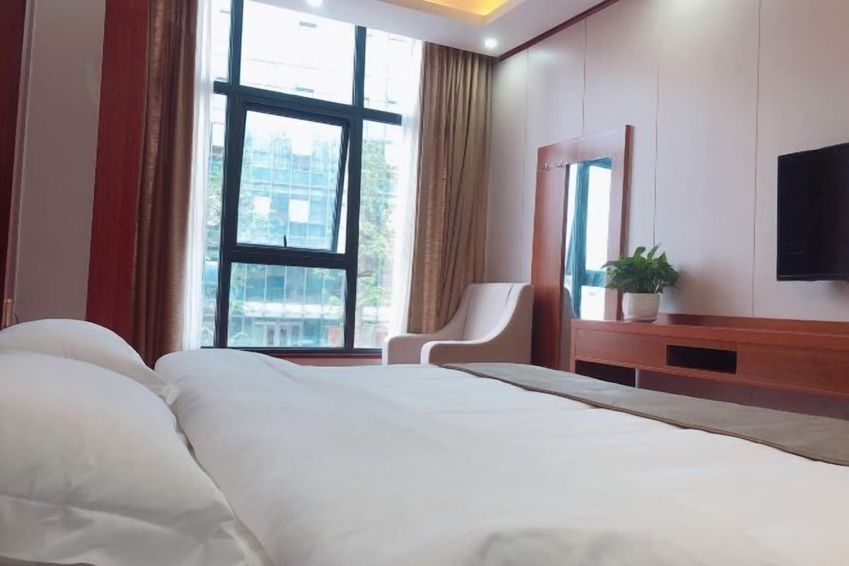 A hotel room with a large bed, a chair, a TV, and a window with curtains.