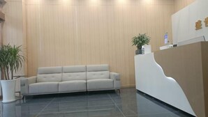 Un área de recepción con un mostrador moderno, un espacio de estar con asientos acolchados y una planta en maceta.