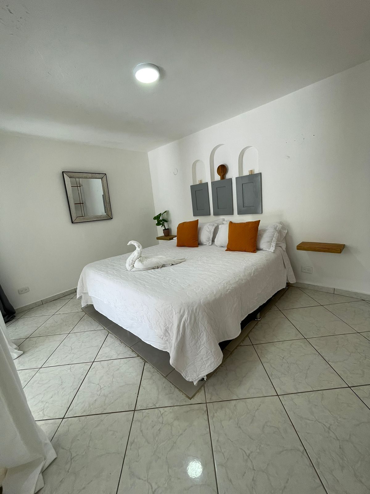 Un dormitorio con una cama grande, paredes blancas, un espejo y una lámpara en el techo.