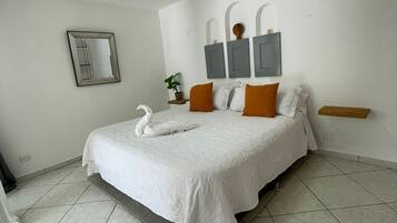 Un dormitorio con una cama grande, paredes blancas, un espejo y una lámpara en el techo.