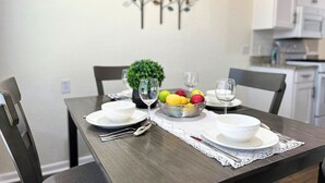 Een eettafel gedekt met borden, kommen, bestek en een schaal fruit.