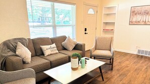 Een woonkamer met een bruine bank, twee fauteuils, een witte salontafel en een deur met uitzicht.