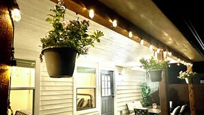 An outdoor patio area with a hot tub, hanging plants, string lights, and outdoor furniture. - Modern 4BR/2B Home, with HotTub, Near DFW Airport (Irving)