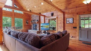 A cozy cabin interior with a large wooden sofa, a fireplace, and a television.