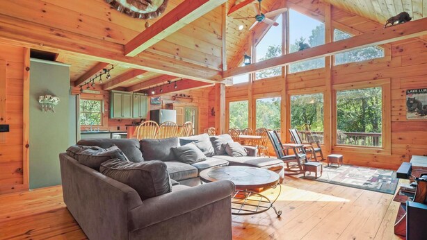A spacious cabin with a large gray sectional sofa, wooden floors, and large windows offering views of the outdoors.