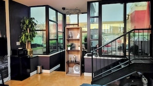Una sala de estar moderna con ventanas amplias, una escalera negra y una estantería de madera.