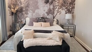 Un dormitorio con una cama grande, una mesita de noche, una lámpara y un mural en la pared.