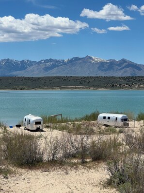 Two RVs parked by a lake with mountains in the background.