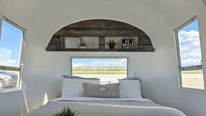 A bedroom with a bed, a skylight, a window, a bench, and a plant. - Firepit-Shade-Chairs-Dark Skies (Levan)