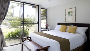 Une chambre d’hôtel avec un grand lit, un banc, une fenêtre donnant sur un espace verdoyant et un ventilateur de plafond.