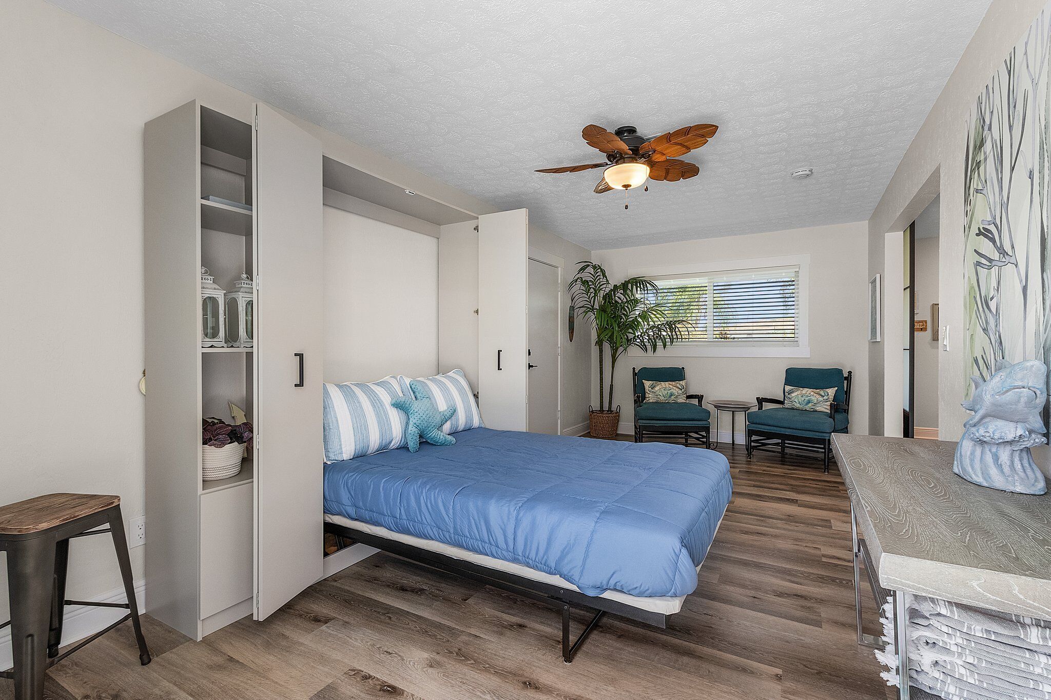 A bedroom with a bed, a ceiling fan, a desk, a chair, and a window with blinds.