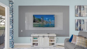 Un salon avec un téléviseur fixé au mur, un canapé gris, un tapis à motifs et un meuble de rangement blanc.