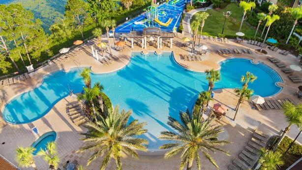 Une grande piscine extérieure divisée en plusieurs zones, entourée de palmiers et de chaises longues.