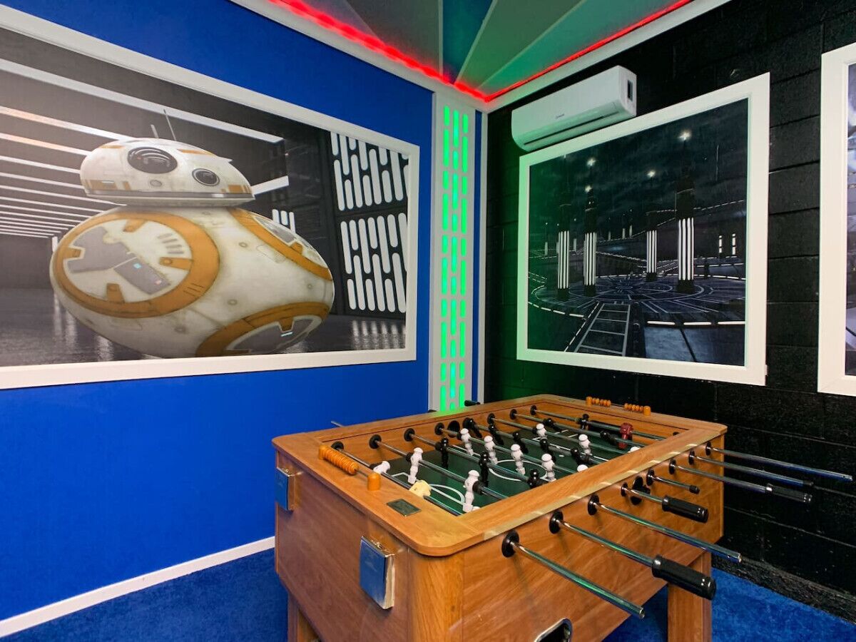 A room with a foosball table, a large poster of a droid, and a window with a view of a cityscape.