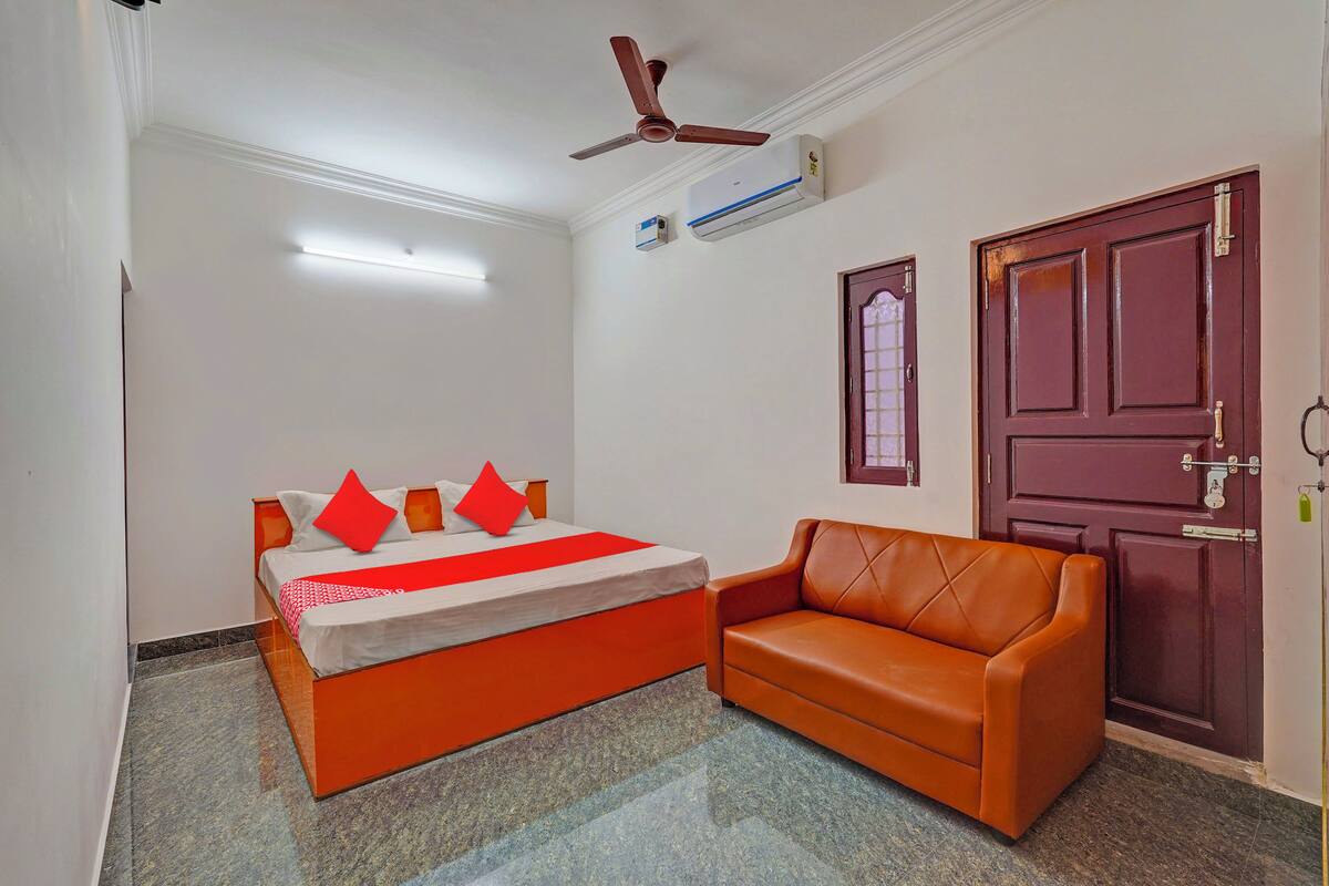 A bedroom with a bed, a sofa, a ceiling fan, an air conditioning unit, and a door.