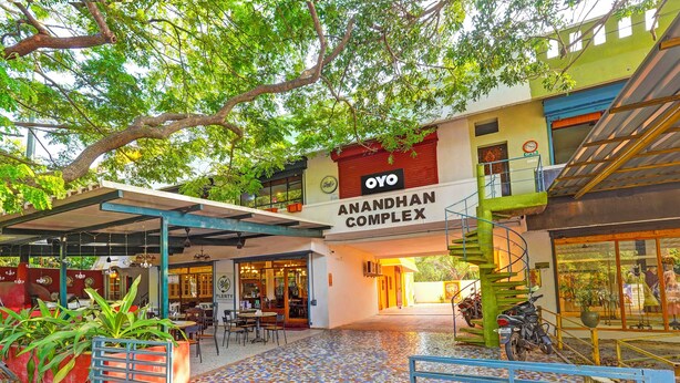 Uma área externa coberta com piso de azulejos, uma escadaria e uma placa indicando o OYO Anandhan Complex.