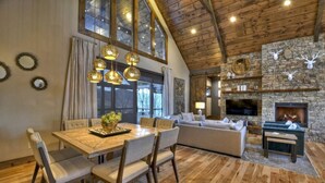 A spacious living area with a stone fireplace, wooden ceiling, and a dining table with chairs.