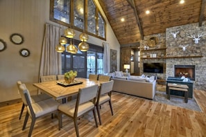 Àmplia zona d'estar amb una llar de pedra, sostre de fusta i taula de dinar amb cadires.