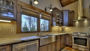 A modern kitchen with stainless steel appliances, wooden cabinets, and a large window providing natural light.
