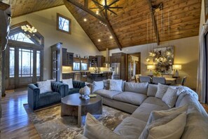A spacious living area with a high ceiling, a large sofa, a coffee table, and a kitchen in the background.