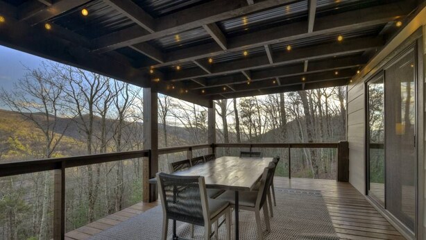 An outdoor deck with a table and chairs, overlooking a forested landscape.