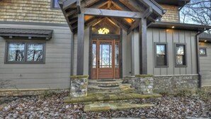 A house with a stone foundation, a wooden front porch, and a central door with a light fixture above.