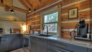 A modern kitchen with dark cabinets, stainless steel appliances, and a window providing a view of the outdoors. - Hygge House | Cozy Cabin + Fire Pit Near Downtown (Blue Ridge)