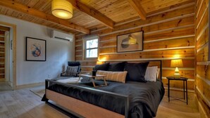 A log cabin bedroom with a bed, bedside lamps, and framed artwork on the walls. - Hygge House | Cozy Cabin + Fire Pit Near Downtown (Blue Ridge)