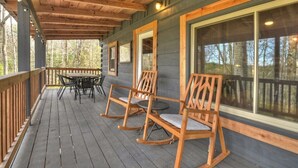 A wooden deck with a table and chairs, large windows, and a view of trees. - Hygge House | Cozy Cabin + Fire Pit Near Downtown (Blue Ridge)