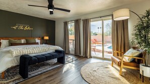Un dormitorio con cama, un banco, un escritorio, una planta y vistas al exterior.