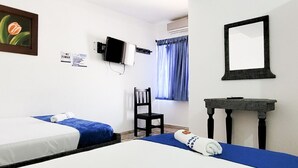 A hotel room with two beds, a chair, a small table, a television, and a window with curtains.