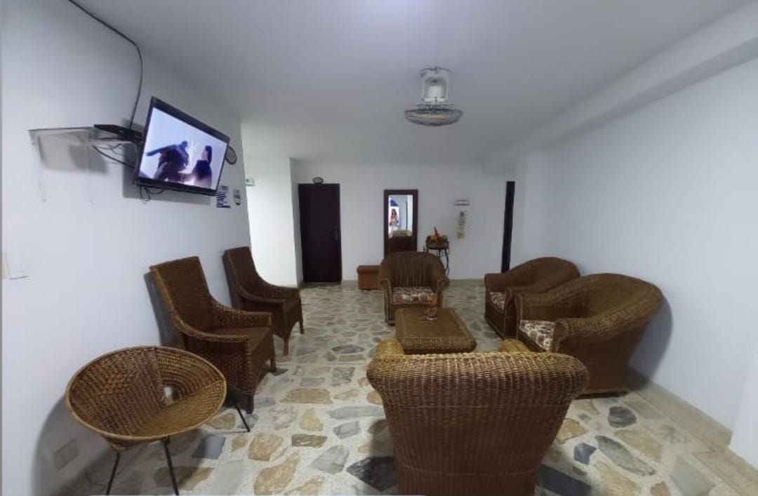 Sala de espera con mobiliario de mimbre, un televisor y suelo de piedra.