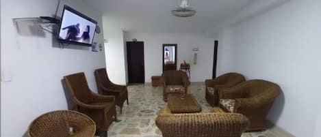 Sala de espera con mobiliario de mimbre, un televisor y suelo de piedra.