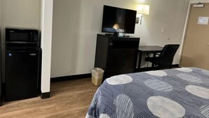 A hotel room with a bed, a desk with a chair, a television, and a microwave. - Hilltop Inn (Conley)
