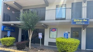 A hotel with a sign for the Hilltop Inn Office, a staircase leading to the entrance, and a parking sign indicating guest parking. - Hilltop Inn (Conley)