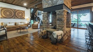 A spacious living area with a stone fireplace, wooden flooring, a sofa, and a bar area. - Stag's Manor|Stunning Mtn Views|Game Room|Hot Tub (Morganton)
