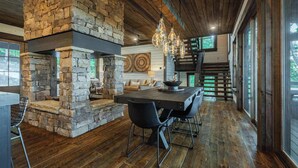 A rustic interior with a stone fireplace, wooden flooring, and a dining area with chairs. - Stag's Manor|Stunning Mtn Views|Game Room|Hot Tub (Morganton)