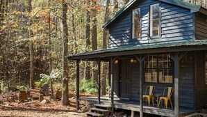 Un chalet rustique doté d’une véranda, de chaises en bois et surplombant une forêt.