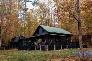 A cabin with a porch and a staircase, surrounded by trees with autumn foliage.