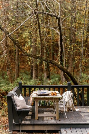 An outdoor seating area with a bench and a table, surrounded by a forest. - Holden Haus | Creekside Cabin + Hot Tub + Dogs (Ellijay)