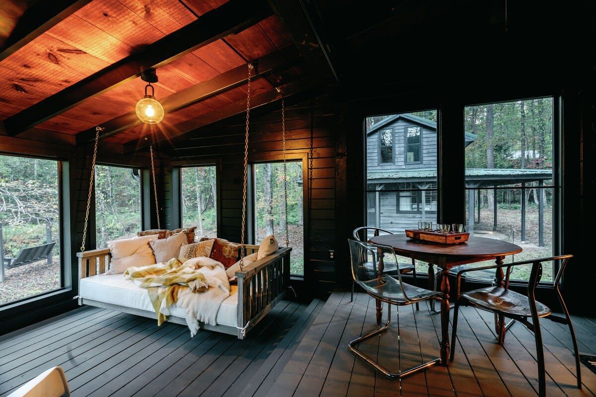 Interior de cabana de madeira com balanço, mesa de jantar e cadeiras.