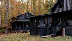 Een chalet met een veranda en buitentrap, omringd door bomen met herfstkleuren.