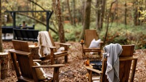 Een rustieke buitenruimte met houten stoelen en tafels, omringd door bomen.