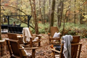 A rustic outdoor seating area with wooden chairs and tables, surrounded by trees. - Holden Haus | Creekside Cabin + Hot Tub + Dogs (Ellijay)